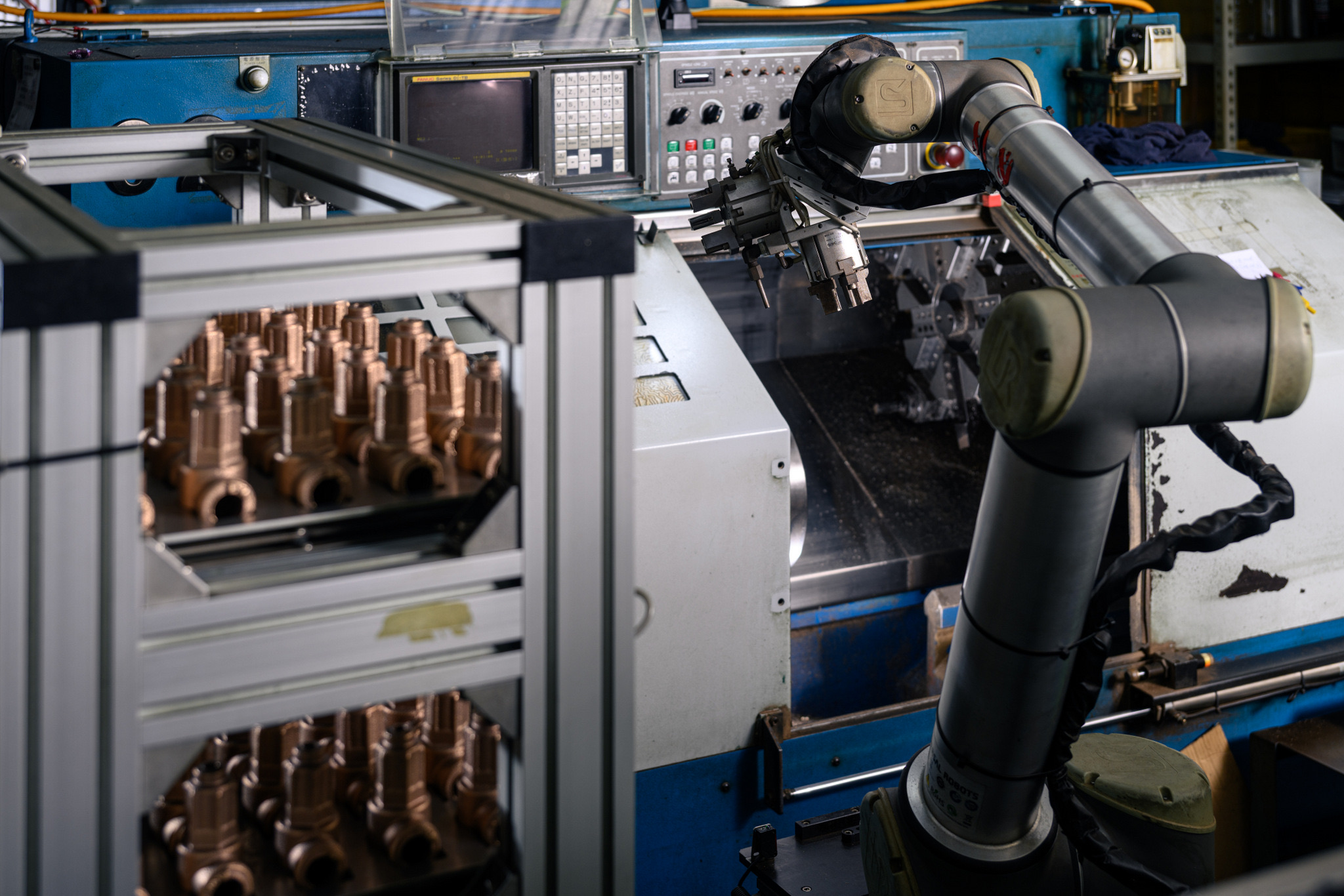 A robot arm tending a CNC lathe next to racks of brass valve bodies